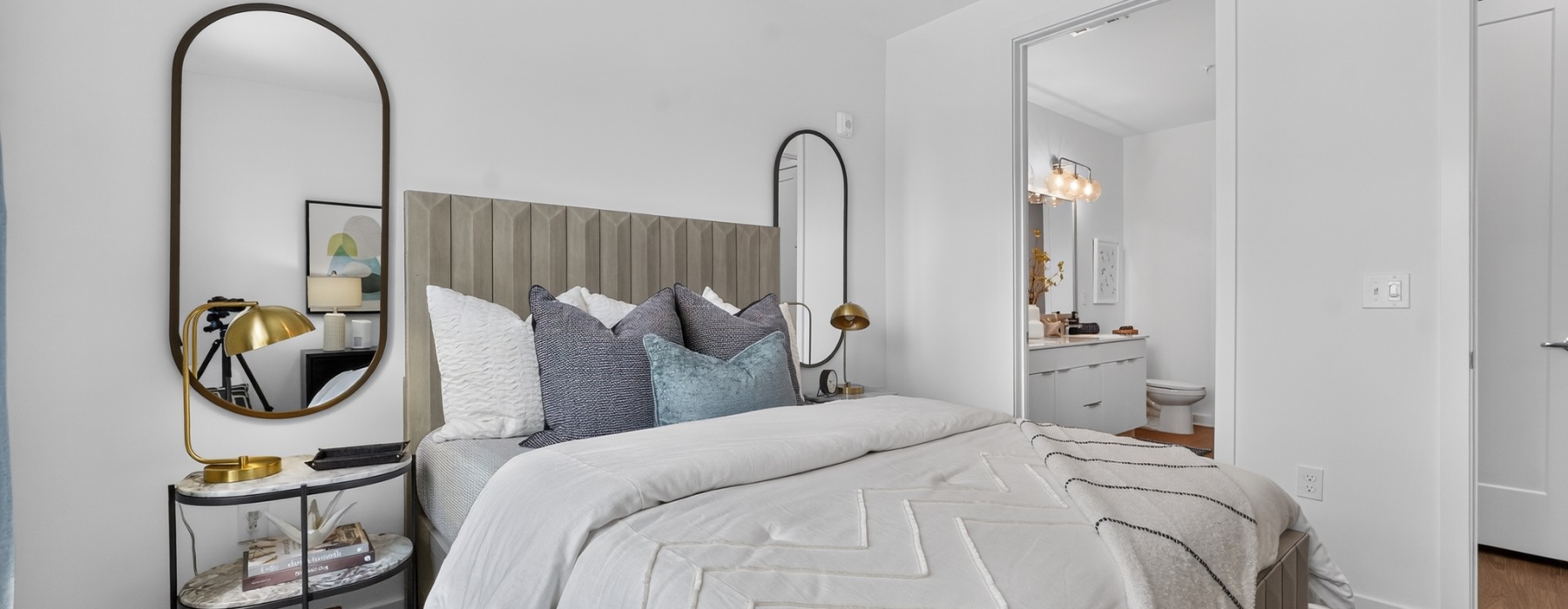 Bedroom in a One Riverside one-bedroom apartment in Jacksonville, FL with tan upholstered headboard and round mirrors